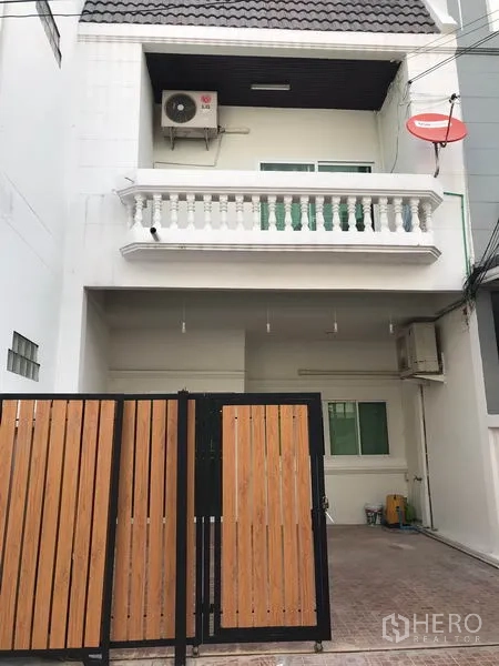 Townhouse for rent or sale in Phra Khanong, Bangkok - White multi-storey townhouse facade with gated carport and balcony.