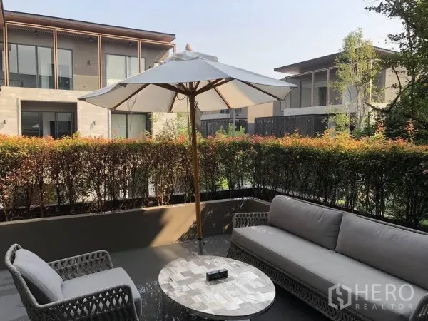 Detached House for sale in Bang Kapi, Bangkok - Private patio lounge with umbrella, wicker seating and trimmed hedges overlooking modern neighboring homes.