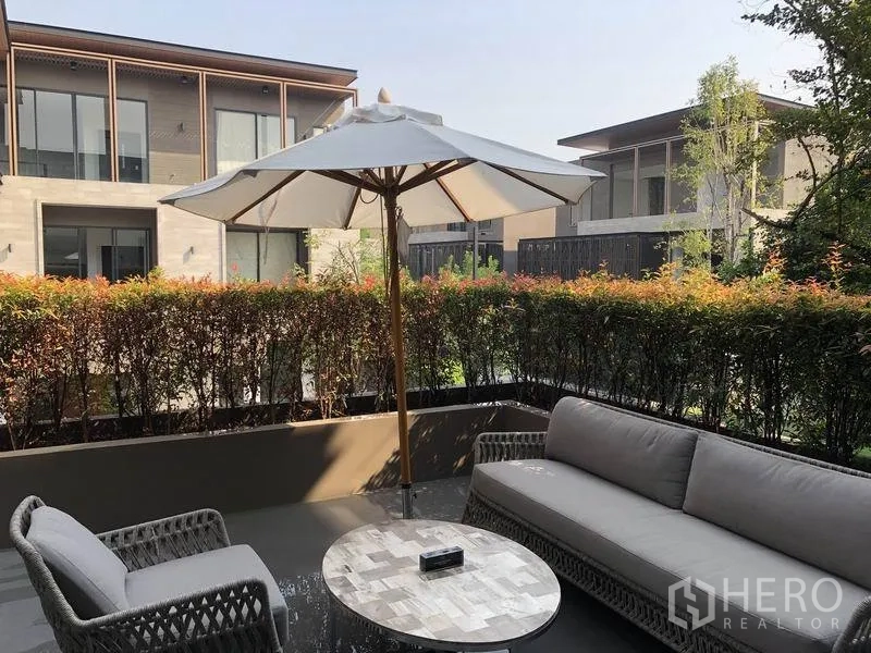 Detached House for sale in Bang Kapi, Bangkok - Private patio lounge with umbrella, wicker seating and trimmed hedges overlooking modern neighboring homes.