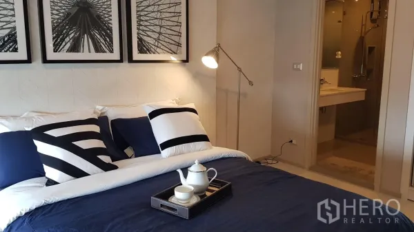 Condominium for rent in Khlong Toei, Bangkok - Cozy bedroom with navy bedding, monochrome art and an ensuite bathroom.
