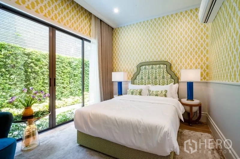 Detached House for sale in Bang Kapi, Bangkok - Garden-view bedroom with sliding glass doors, patterned wallpaper and bedside lamps.