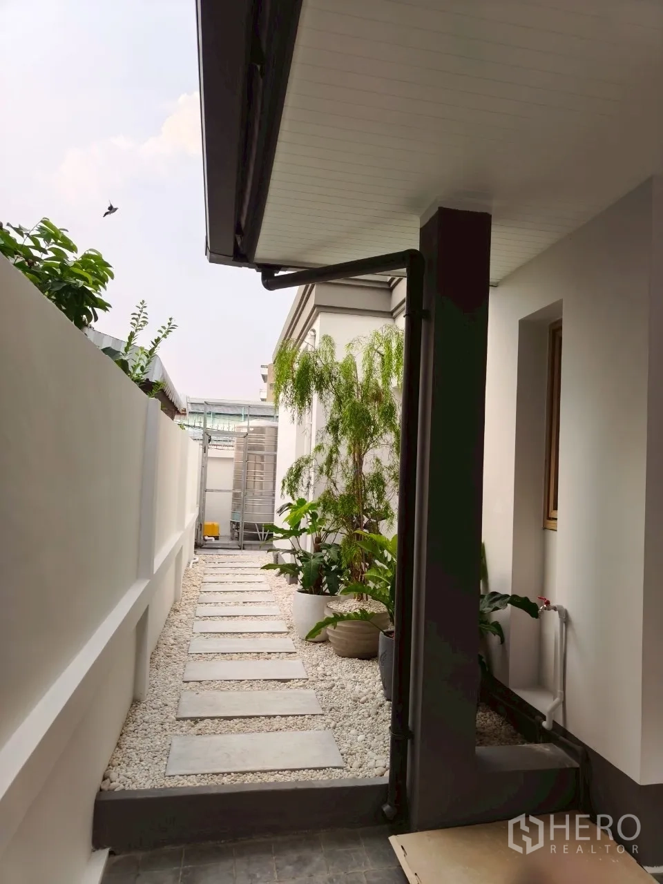 Detached House for sale in Suan Luang, Bangkok - Side walkway with stepping stones, white pebbles and potted greenery.