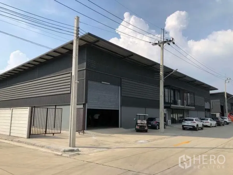 Warehouse for rent in Bang Phli, Samut Prakan - Modern grey warehouse exterior in Bang Phli with large roller shutter, wide concrete road and parking.