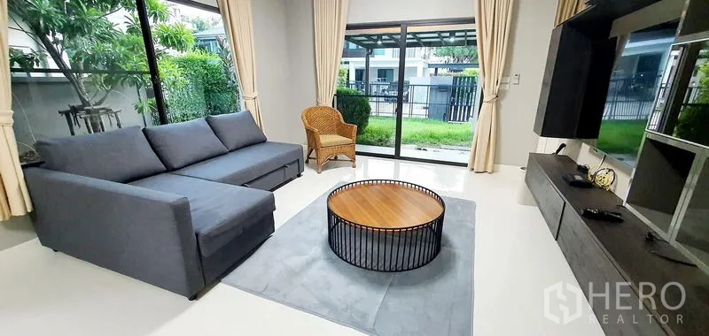 Detached House for rent in Bang Phli, Samut Prakan - Lounge with gray sofa and round coffee table facing the private garden through sliding doors