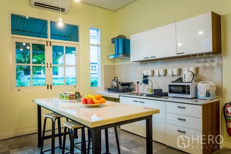 Home Office for rent in Suan Luang, Bangkok - Modern kitchen with island, white cabinetry and windows overlooking greenery.