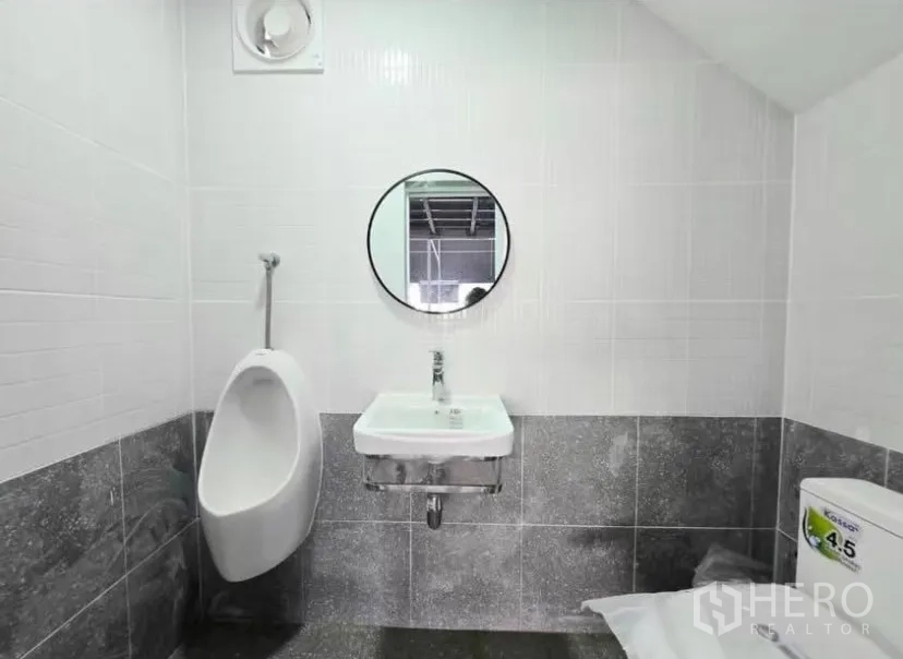 Warehouse for rent in Prawet, Bangkok - Clean tiled restroom with urinal, sink, round mirror and toilet.