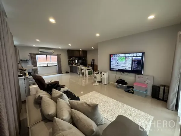 Detached House for rent or sale in Lam Luk Ka, Pathum Thani - Bright living and dining area with large TV wall, windows with curtains and ample natural light.