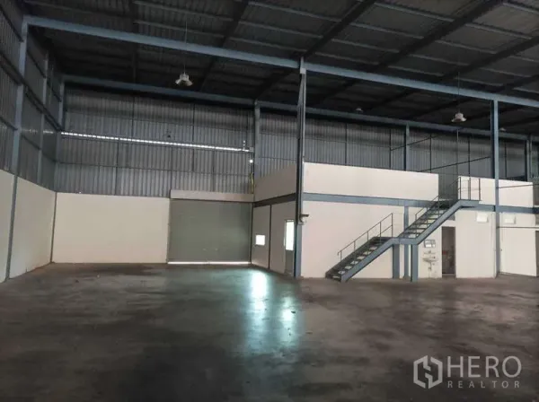 Factory for rent in Ban Phaeo, Samut Sakhon - Spacious warehouse interior with high ceiling, mezzanine office, stairs, and roller-shutter door.