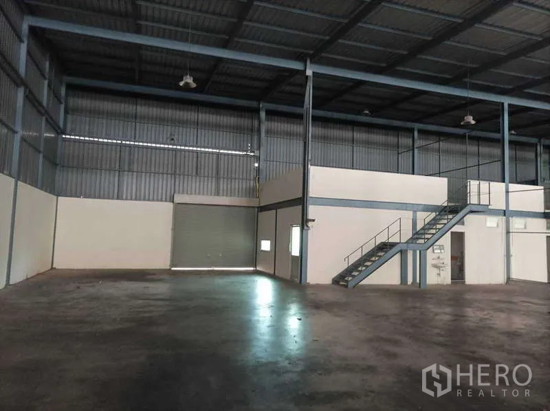 Factory for rent in Ban Phaeo, Samut Sakhon - Spacious warehouse interior with high ceiling, mezzanine office, stairs, and roller-shutter door.