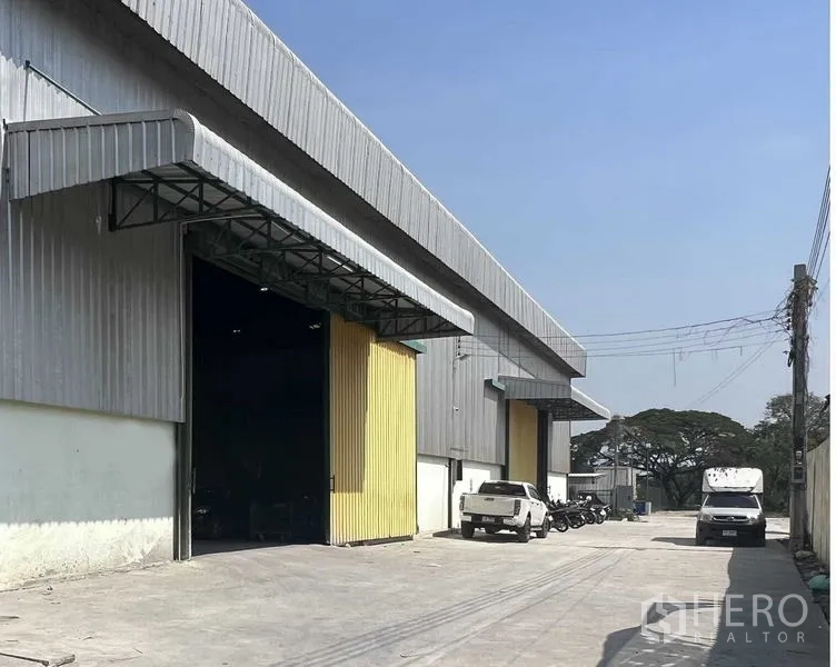 Warehouse for rent in Lat Krabang, Bangkok - Wide concrete driveway and multiple warehouse bays with open yellow doors and steel awnings for truck access.