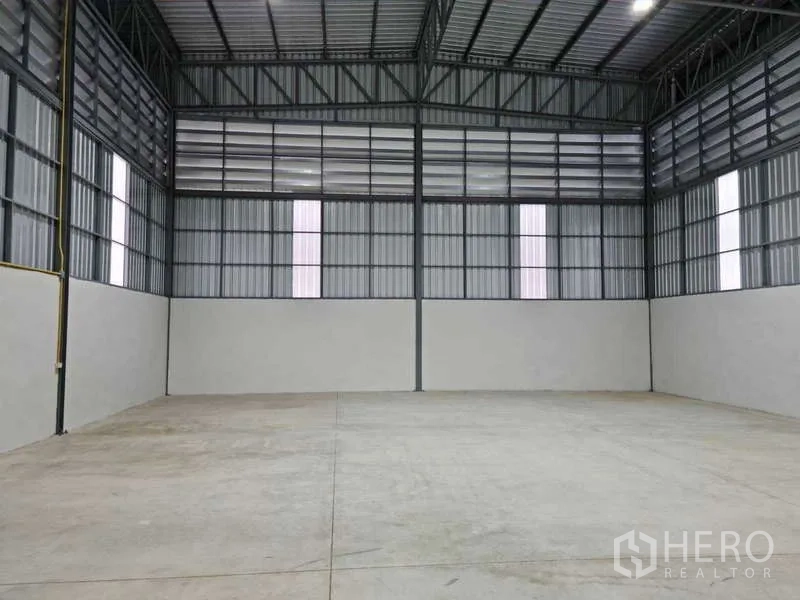 Warehouse for rent in Bang Bua Thong, Nonthaburi - Front compound view with parking space, vans and trucks outside a new metal-clad warehouse.