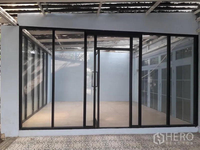 Detached House for rent in Watthana, Bangkok - Glass-enclosed room with black aluminum sliding doors opening to a tiled patio.