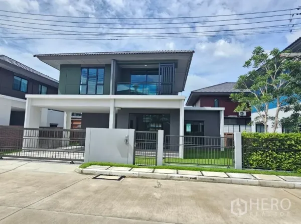 Detached House for sale in Lam Luk Ka, Pathum Thani - Front elevation of the house showing balcony, fence and green lawn.