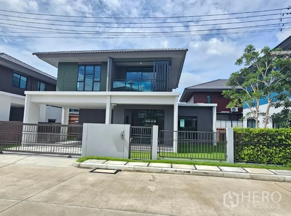Detached House for sale in Lam Luk Ka, Pathum Thani - Front elevation of the house showing balcony, fence and green lawn.