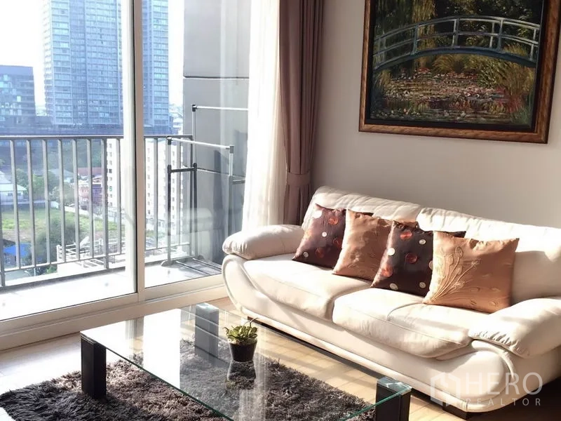 Condominium for rent in Khlong Toei, Bangkok - Sofa beside floor-to-ceiling sliding doors opening to a balcony with skyline view.