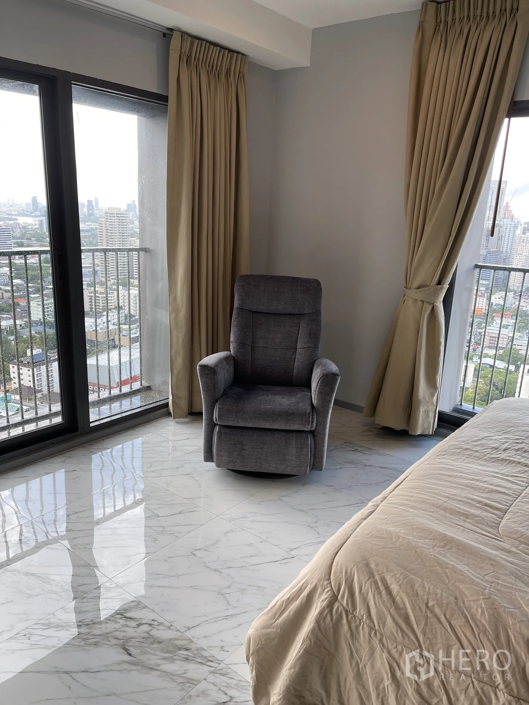 Condominium for rent in Khlong Toei, Bangkok - Reading corner with gray recliner beside two balcony doors overlooking the city.