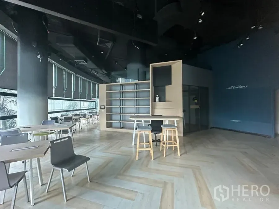 Office Space for rent - Open-plan office with herringbone wood floors, high black ceiling, built-in shelves, island counter and large window shades.