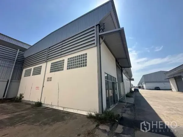 Warehouse for rent in Bang Bua Thong, Nonthaburi - Corner view of the warehouse with glass block windows and a covered side walkway within the compound.
