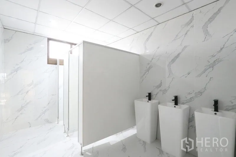 Office Space for rent in Bang Na, Bangkok - Restroom with three pedestal sinks, partitions and marble‑style wall tiles.