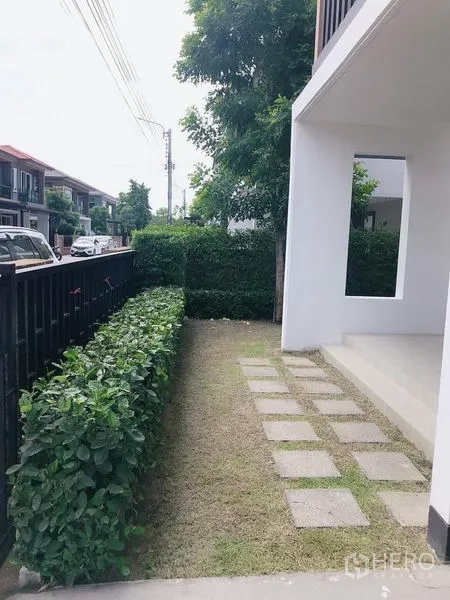 独立式住宅 出售在Suan Luang, Bangkok - 前庭步道，铺设踏脚石，旁有黑色围栏与灌木。