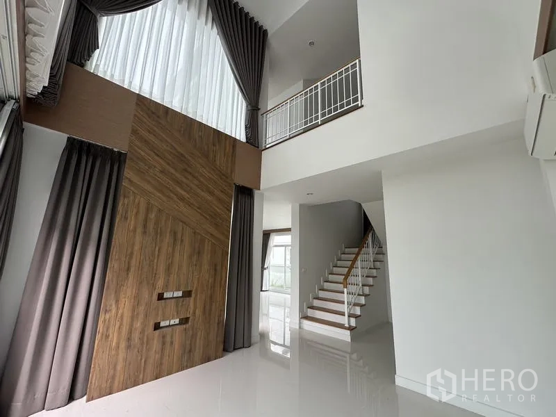 Detached House for sale in Lam Luk Ka, Pathum Thani - Vaulted living area with tall drapes and a wood feature wall.