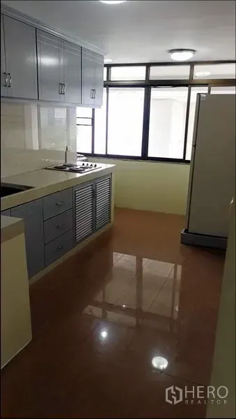 Condominium for rent or sale in Khlong Toei, Bangkok - Separate kitchen with grey cabinets, cooktop, sink, refrigerator, and large windows.