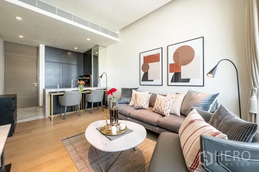 Condominium for rent in Bang Rak, Bangkok - Open-plan living and dining area with grey sofa, marble coffee table, and sleek kitchenette.
