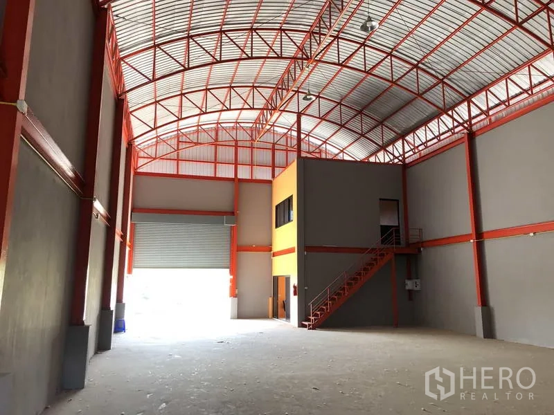 Warehouse for rent in Nonthaburi - Interior view with roller shutter loading bay and mezzanine office box connected by a steel staircase.