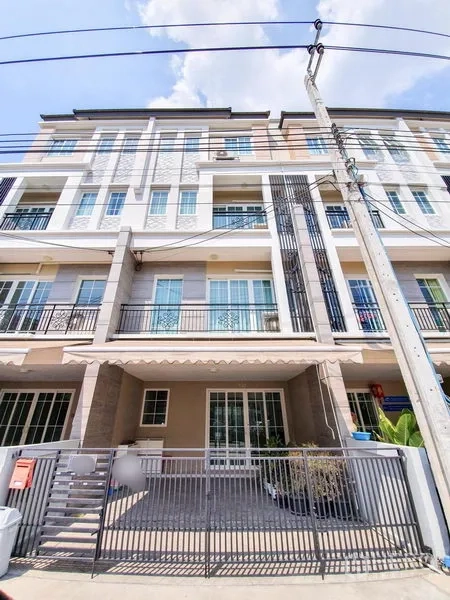 Townhouse for rent in Bang Na, Bangkok - Modern multi-storey townhouse facade with balconies, sliding doors and a gated driveway under blue sky.