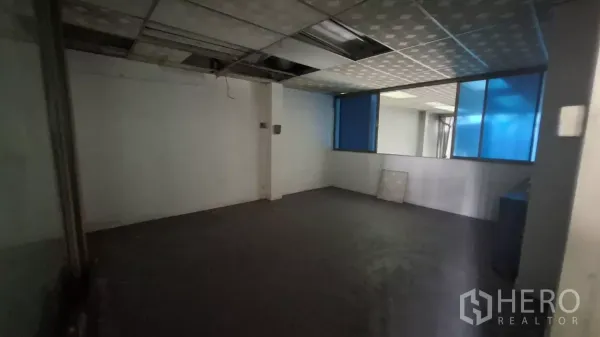 Shophouse for rent in Watthana, Bangkok - Large office room with blue-tinted windows and suspended ceiling panels.