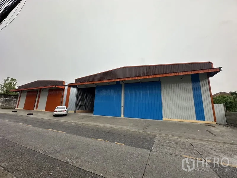 Warehouse for rent in Bueng Kum, Bangkok - Front elevation of large blue-and-orange warehouse bays with high gable roofs and sliding steel doors.