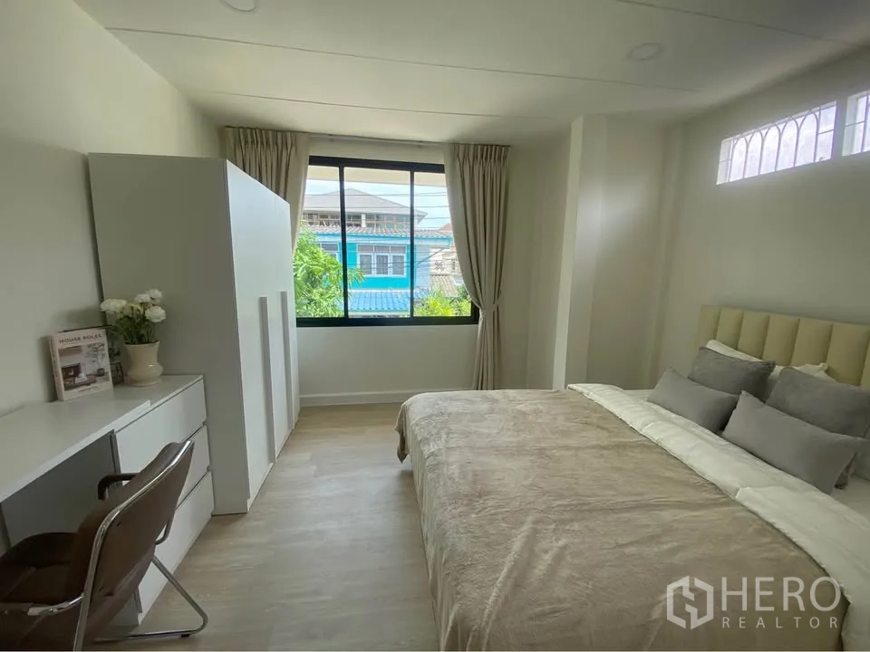 Detached House for rent in Huai Khwang, Bangkok - Bright bedroom with large window, desk, wardrobe and double bed in neutral tones.
