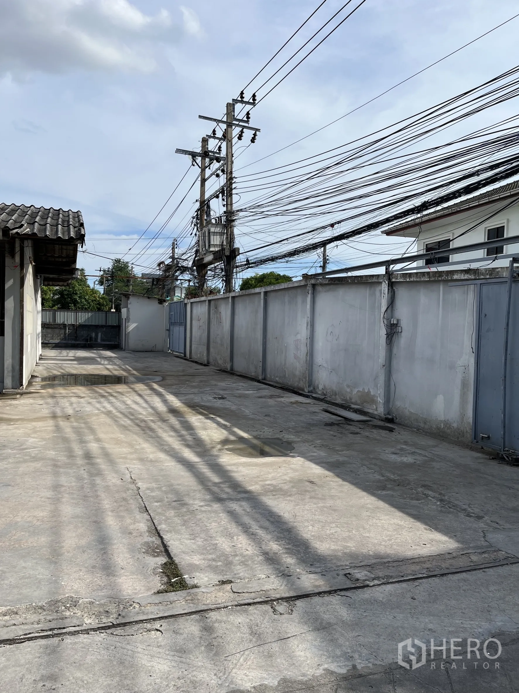 Warehouse for rent in Bangkok - Side driveway and fenced concrete yard with utility poles and power lines.
