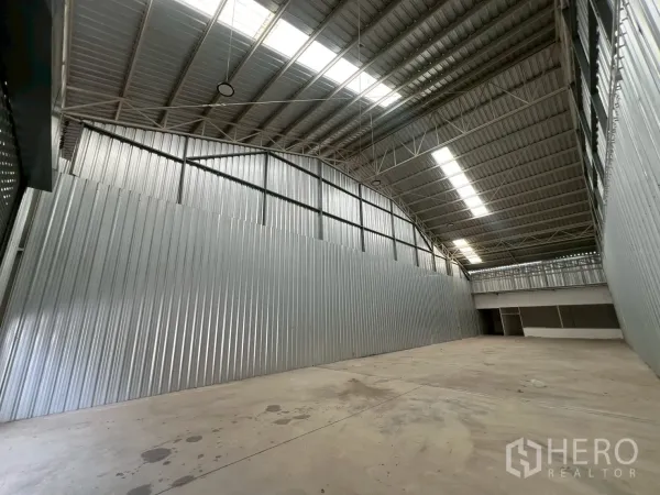 Warehouse for rent in Min Buri, Bangkok - Wide storage hall with high-bay lighting, steel trusses, skylights, and a rear partitioned area.