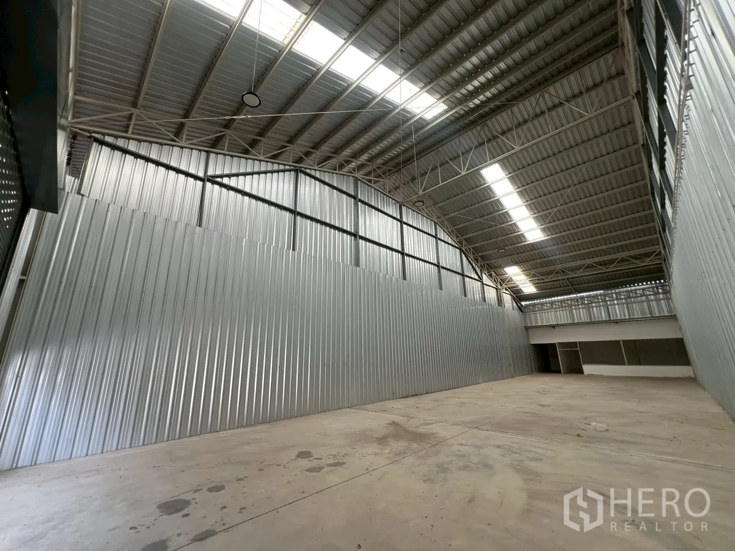 Warehouse for rent in Min Buri, Bangkok - Wide storage hall with high-bay lighting, steel trusses, skylights, and a rear partitioned area.