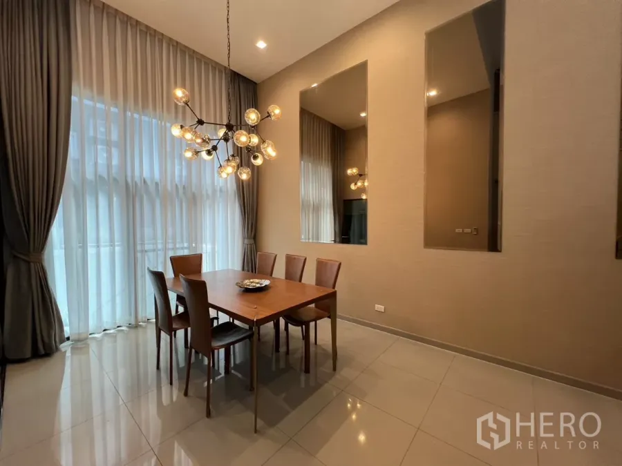 Townhouse for rent in Suan Luang, Bangkok - Dining area with modern chandelier, tall sheer curtains and a six-seat wooden table.