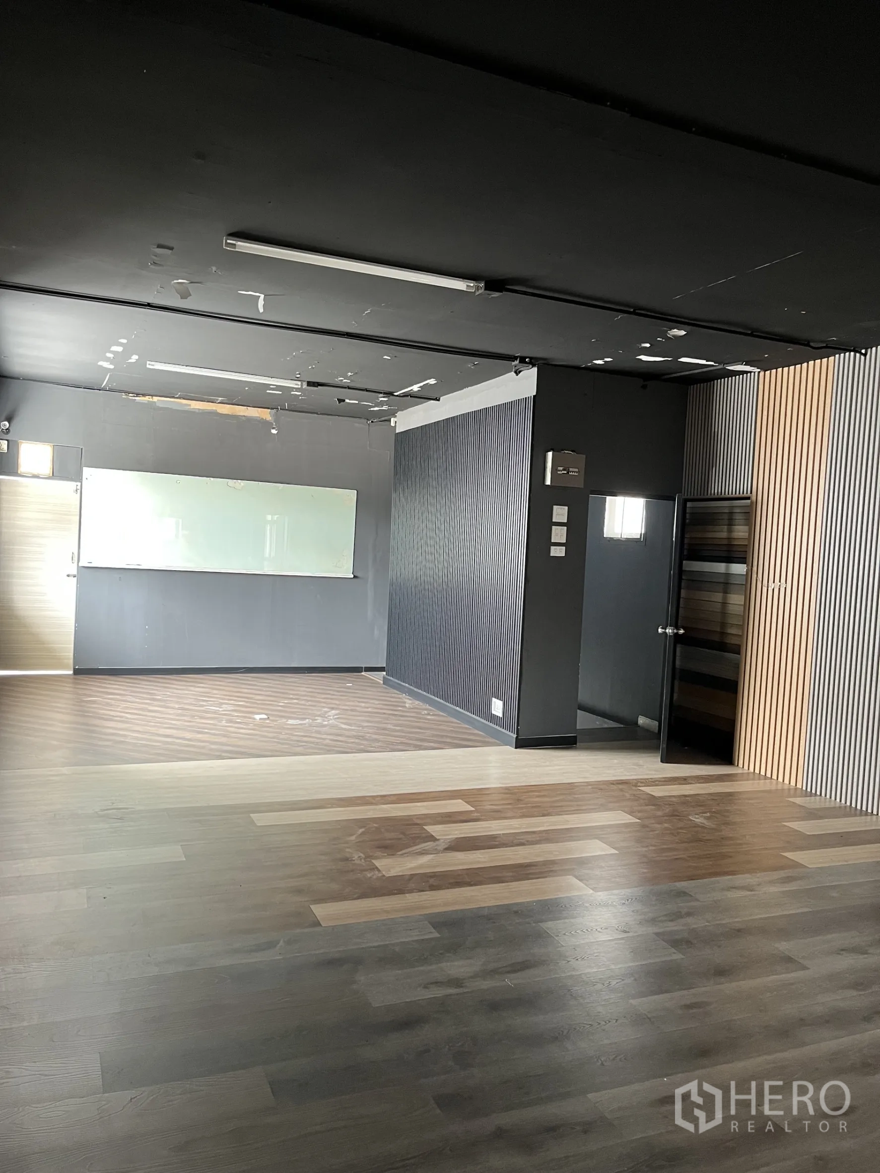 Warehouse for rent in Bangkok - Large office area with black ceiling, striped wall panels and laminate floors.