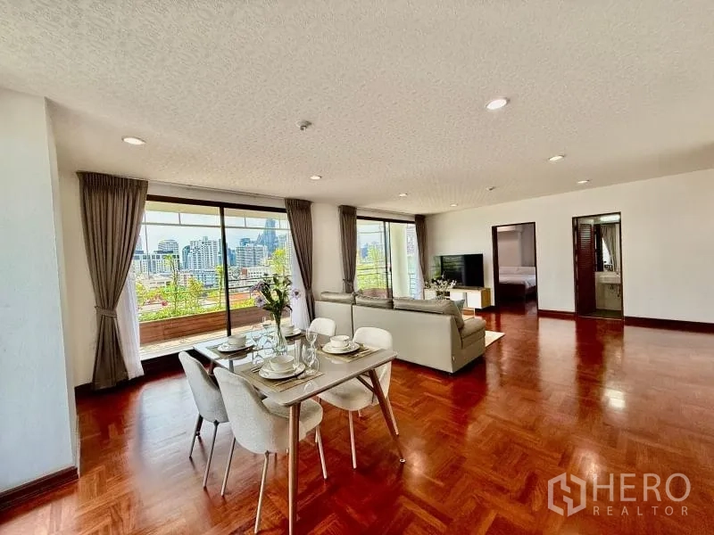 Condominium for rent - Open-plan living and dining area with parquet wood floors, large windows, and a balcony showcasing city views.