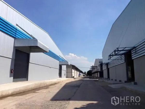 Warehouse for rent in Phra Nakhon Si Ayutthaya - Row of modern warehouses along a wide driveway with loading docks and roller shutters.