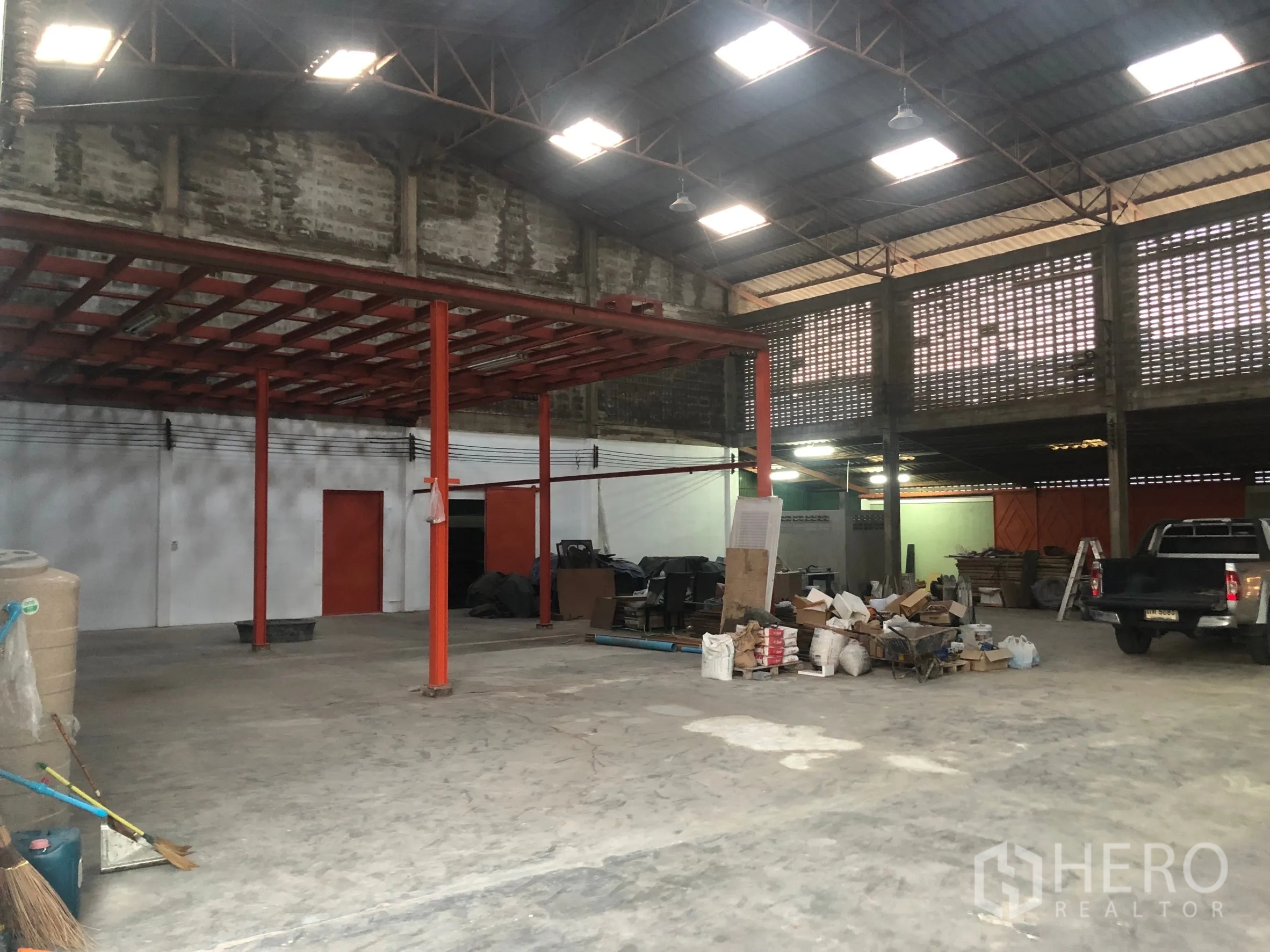 Warehouse for rent in Min Buri, Bangkok - Large storage hall with red steel columns, partial mezzanine frame and wide loading space on concrete floor.