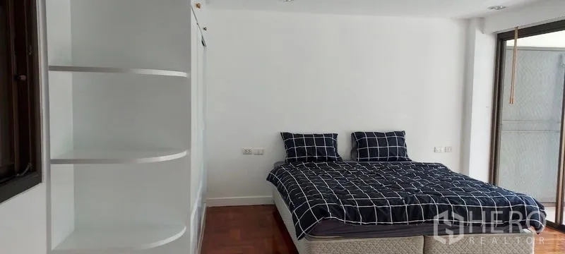 Townhouse for rent in Sathon, Bangkok - Guest bedroom with curved shelving, glossy wooden flooring and balcony access.