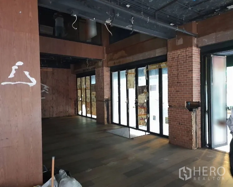 Shophouse for rent - Spacious retail hall with brick columns, floor-to-ceiling windows and wood-look floors.