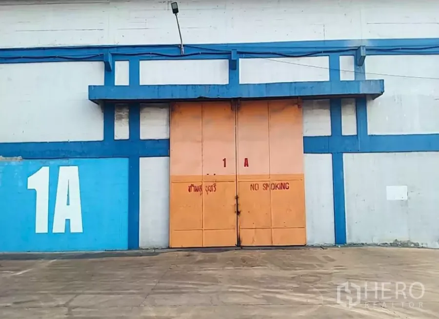Factory for rent in Phra Pradaeng, Samut Prakan - Industrial unit exterior with wide sliding metal doors and a large loading apron marked 1A.