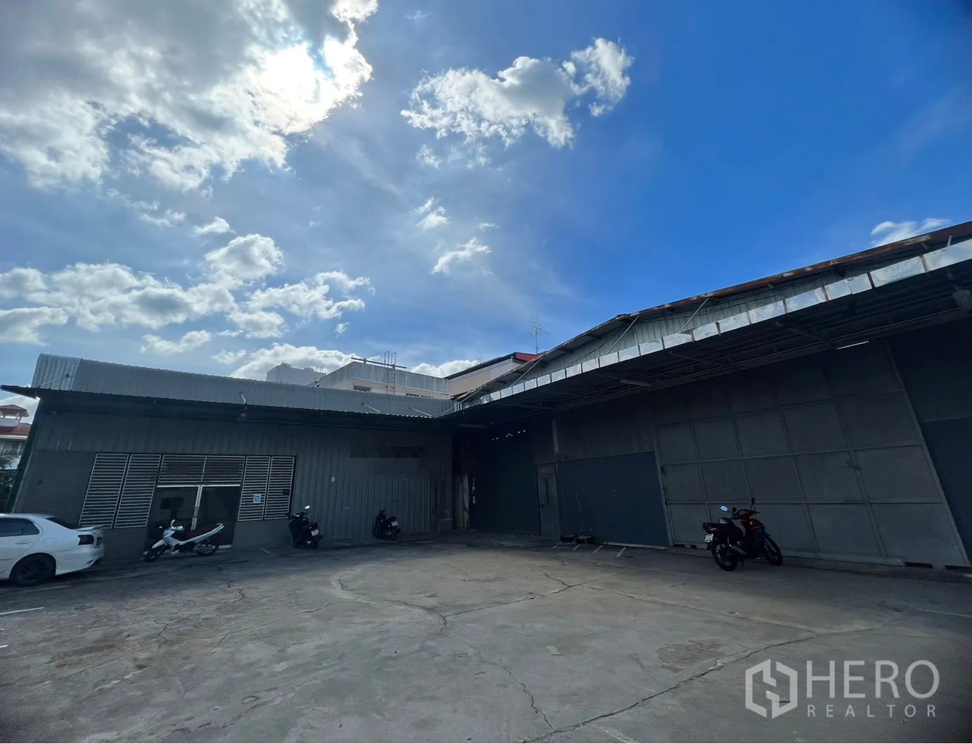 Warehouse for rent in Suan Luang, Bangkok - Metal-clad warehouse exterior in Bangkok with a large concrete loading yard and parking under a bright sky.