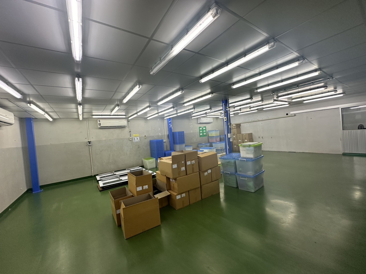 Warehouse for rent or sale in Lam Luk Ka, Pathum Thani - Bright warehouse production room with green epoxy floor, blue columns, air-conditioning and stacked boxes.