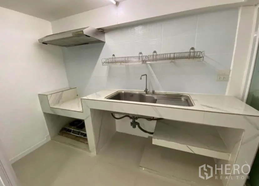 Townhouse for rent in Phra Khanong, Bangkok - Simple Thai kitchen with marble-look counters, large sink, wire racks, and range hood.