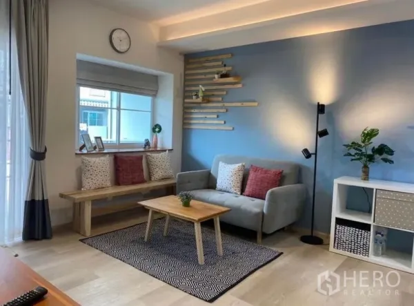 Townhouse for rent in Bang Phli, Samut Prakan - Bright living room in a Bang Phli townhouse with blue feature wall, window bench, grey sofa and wood coffee table.