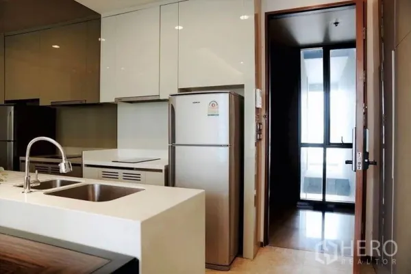 Condominium for rent in Khlong Toei, Bangkok - Sleek kitchen with island sink, glossy cabinets, stainless refrigerator, and door to balcony.
