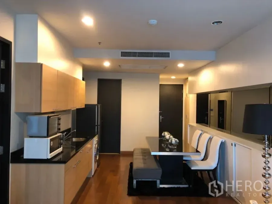 Condominium for rent in Pathum Wan, Bangkok - Open-plan kitchen and dining area with light wood cabinets, black countertops, built-in appliances, and bench seating in a Pathum Wan condo.
