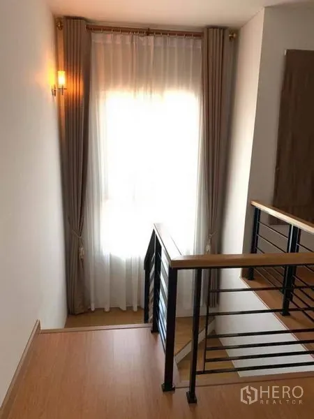 独立式住宅 出售在Suan Luang, Bangkok - 楼梯平台，木扶手与黑色栏杆，窗配纱帘。